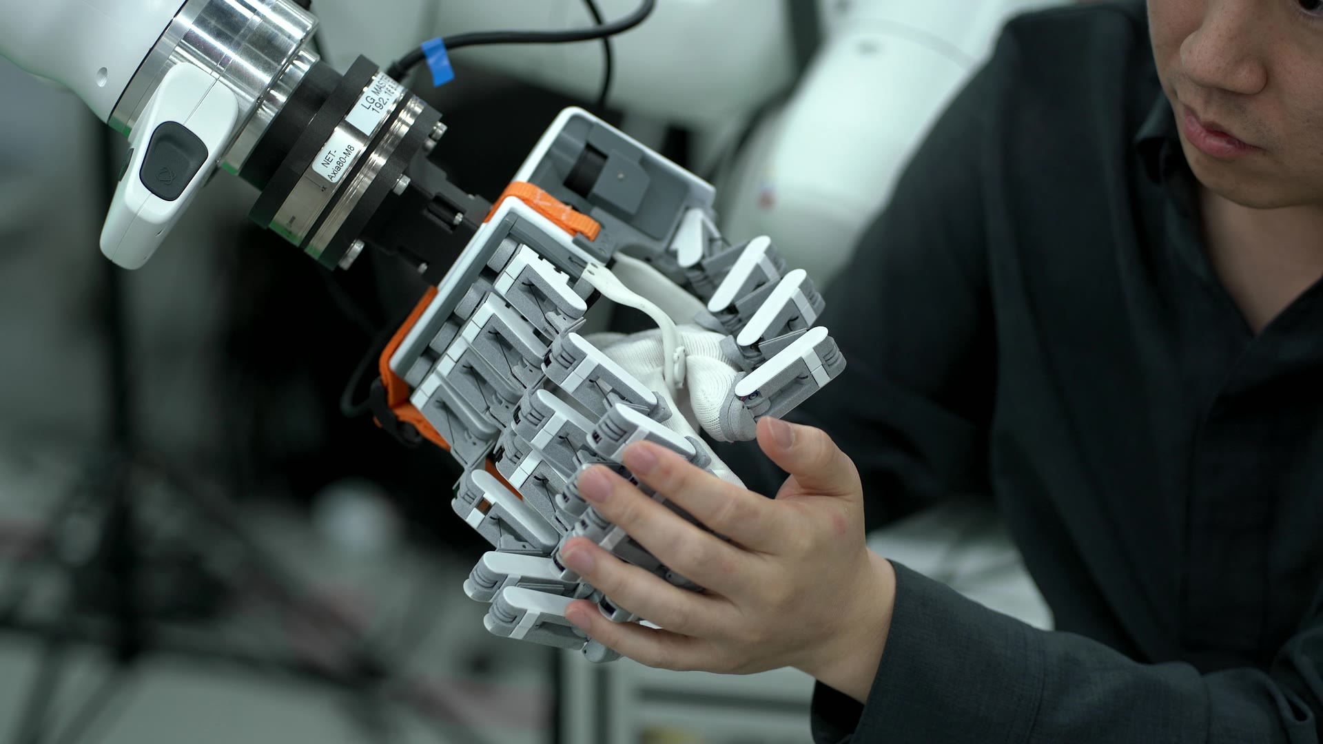 An operator's hand in a master glove, next to the robot arm.